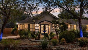 A house with a stone facade, a fountain in the front yard, and a well-maintained garden. - La Mariposa ~ Grand Oasis Big Luxury Home (Sunset Valley Austin)