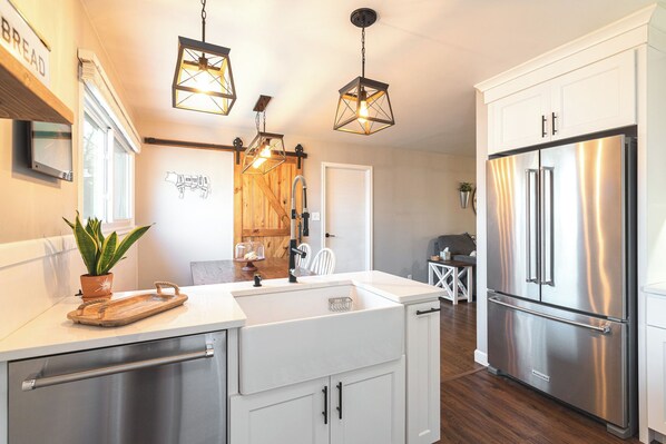 A modern kitchen with white cabinetry, a stainless steel refrigerator, and pendant lighting.