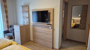 A modern hotel room with a bed, a desk, a TV, and a mirror.