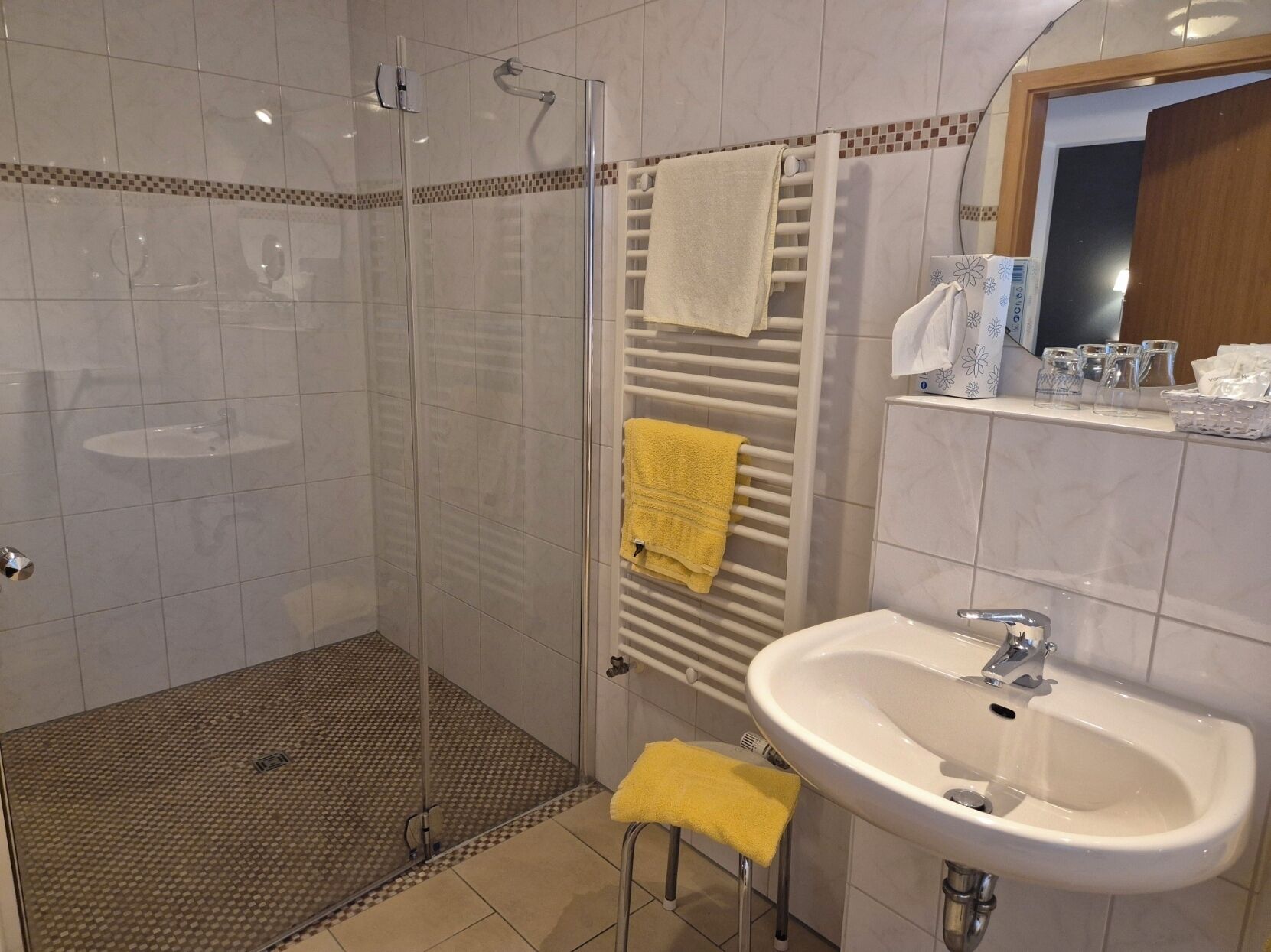 Ein modernes Badezimmer mit einer gläsernen Duschkabine, einem weißen Waschbecken und einem Handtuchhalter mit zwei Handtüchern.