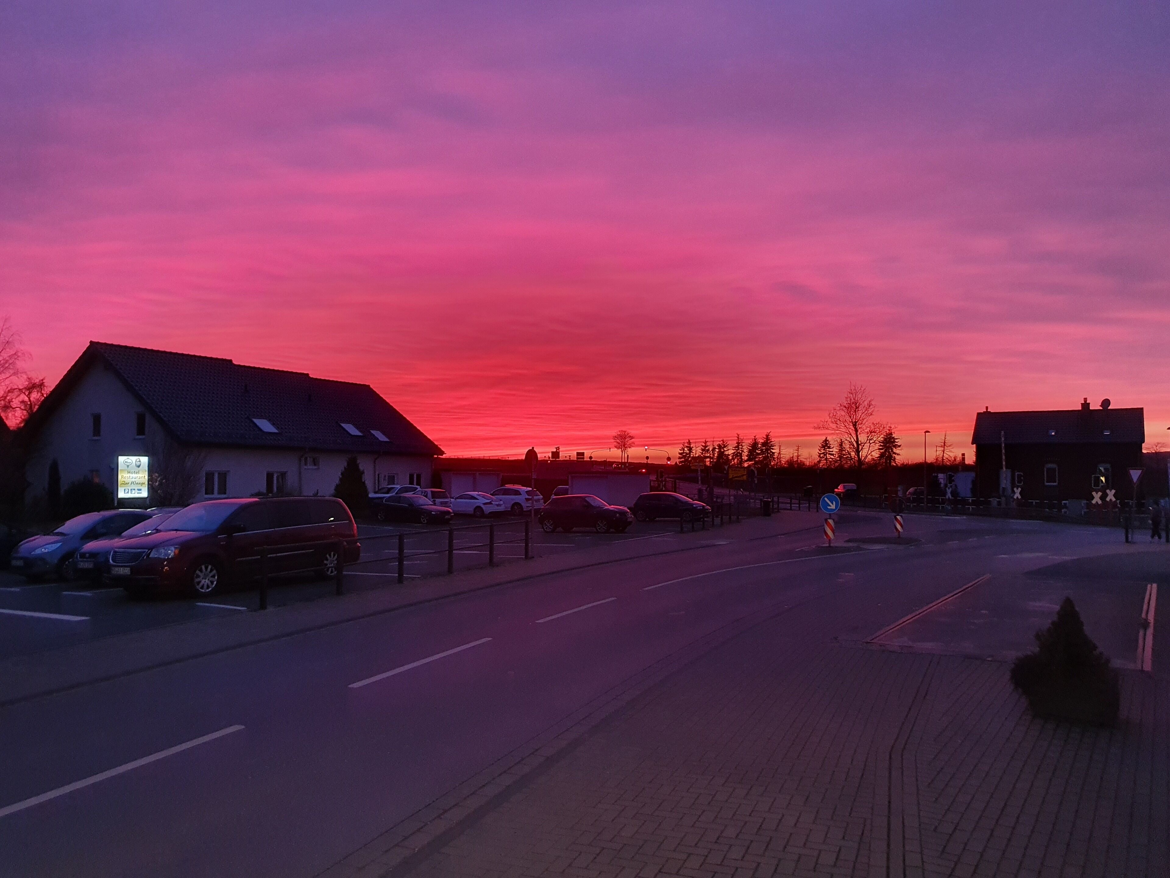 Blick von einer Straße bei Sonnenuntergang, mit einem Hotel links, parkten Autos und einem klaren Himmel.