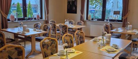 A conference room with multiple tables and chairs, large windows with curtains, and a painting on the wall.