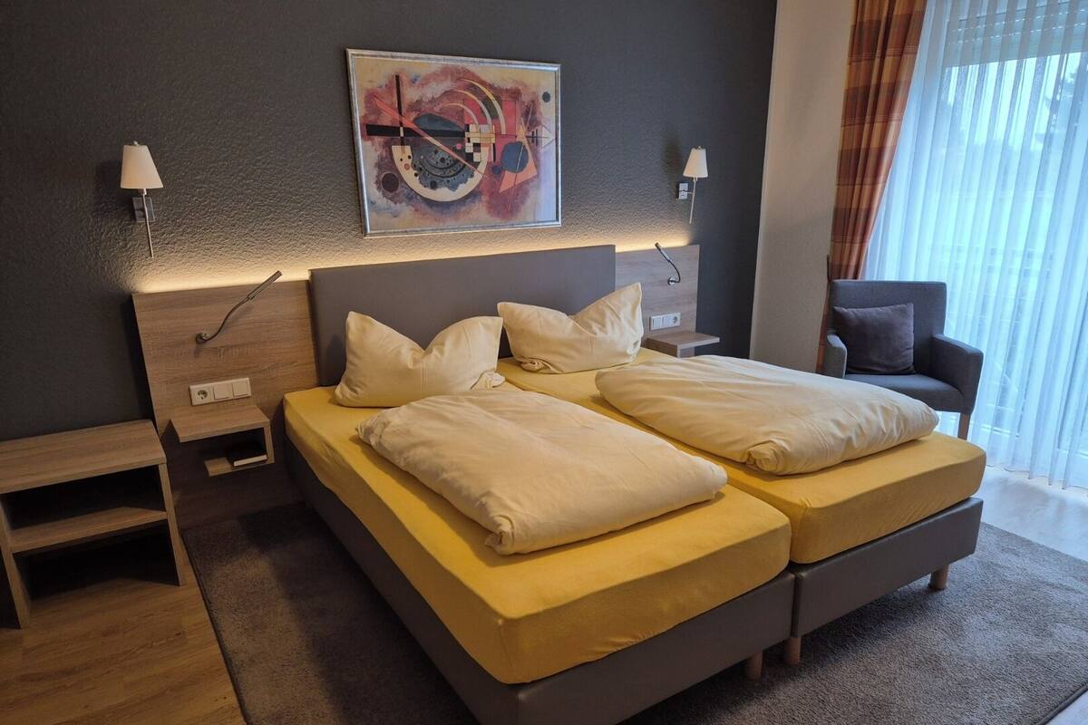A modern hotel room with two beds, a nightstand, a chair, and a painting on the wall.