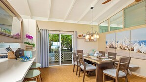 A dining area with a wooden table, chairs, and a view through a glass door to the outdoors. - Oceanview Cottage | Walk to Poipu & Brennecke's Beach (Koloa)