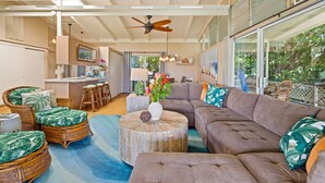 A spacious living area with a large sectional sofa, wicker chairs, a round coffee table, and a ceiling fan. - Oceanview Cottage | Walk to Poipu & Brennecke's Beach (Koloa)