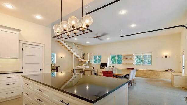 A spacious kitchen with a central island, a dining area with a table and chairs, and a staircase leading to an upper level. - Gorgeous Lakeside BarnHOUSE + SAUNA! (Ashland)