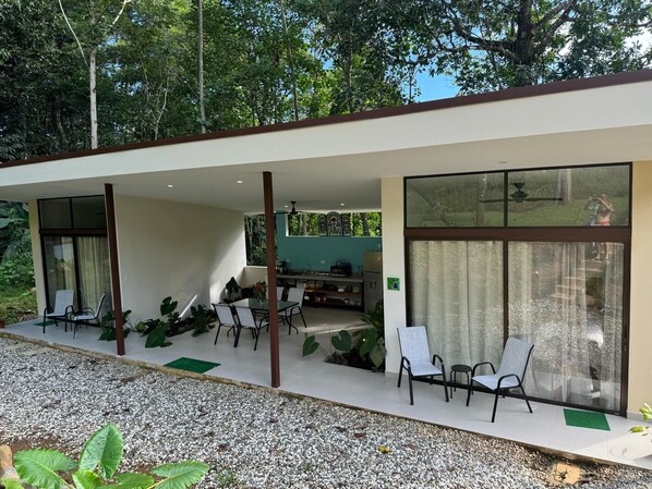 Une maison moderne dotée d’un patio couvert, de grandes fenêtres et offrant une vue sur la verdure environnante.