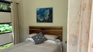 A bedroom with a bed, a ceiling fan, a window with curtains, and a painting on the wall.
