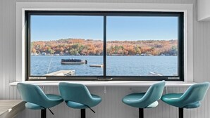 Ein Zimmer mit großem Fenster mit Blick auf einen See und Herbstlaub. Vor dem Fenster stehen drei stahlblaue Sessel.