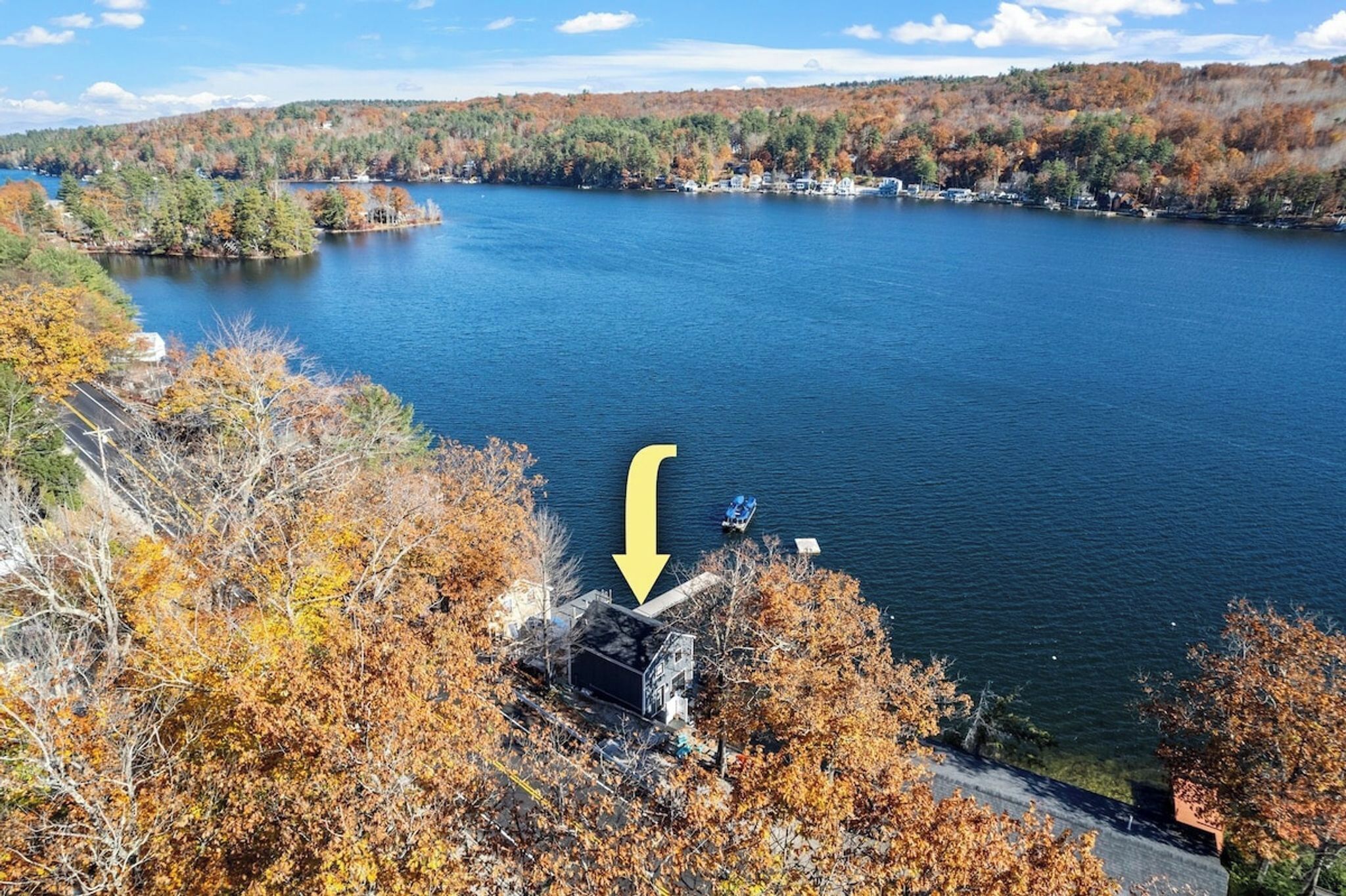 Ein See, umgeben von Herbstlaub, eine Anlegestelle und ein Gebäude, auf das ein gelber Pfeil zeigt.
