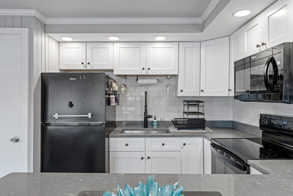 A modern kitchen with white cabinets, a black refrigerator, a stainless steel sink, and a black oven.