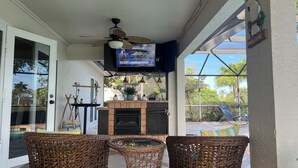 A cozy patio area with wicker furniture, a television mounted on the wall, and a fireplace. - Charming Pool House with a nearly 600 sq/ft Private Efficiency Suite Inside  (Bonita Springs)