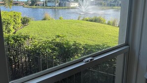 A view through a window of a well-maintained lawn, a body of water, and a distant building. - Charming Pool House with a nearly 600 sq/ft Private Efficiency Suite Inside  (Bonita Springs)