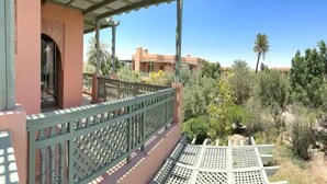 A balcony with a lattice railing overlooking a garden with palm trees and a building in the background. - Magnificent T2 with swimming pool (Marrakech)