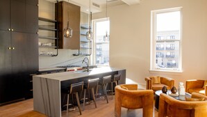 A modern kitchen with a central island, bar stools, and a seating area with sofas. - The Bell Athens by Kasa Living (Athens)