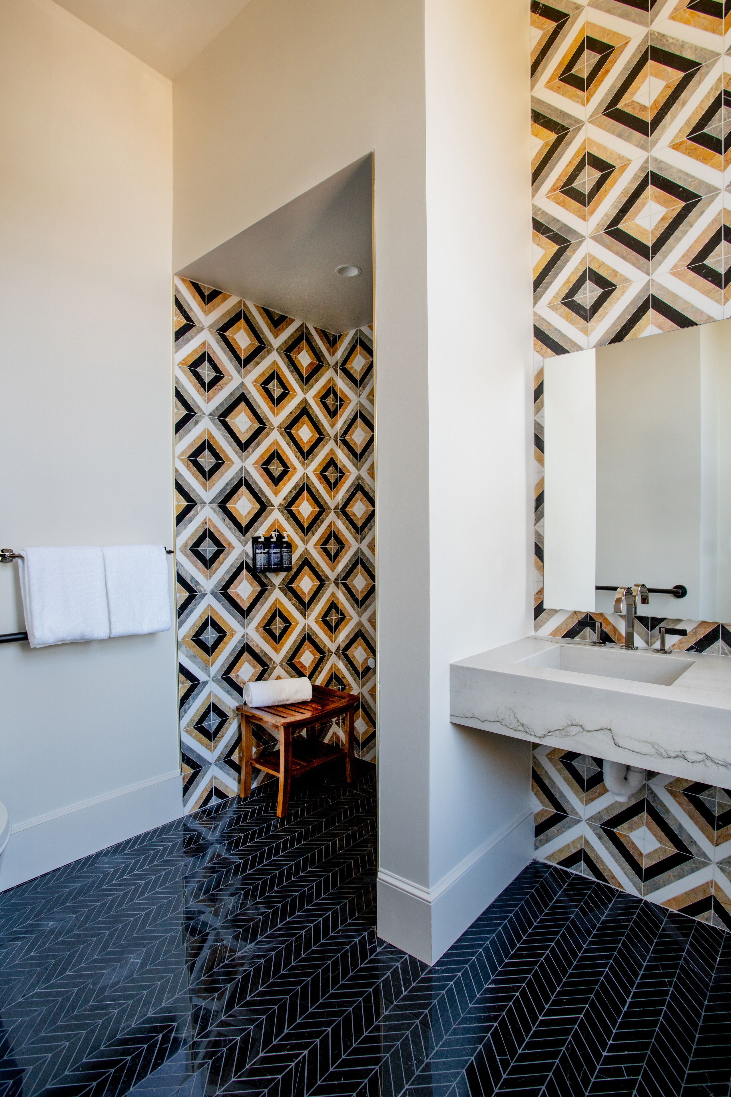 A modern bathroom with a geometric patterned wall, a marble sink, and a herringbone floor.