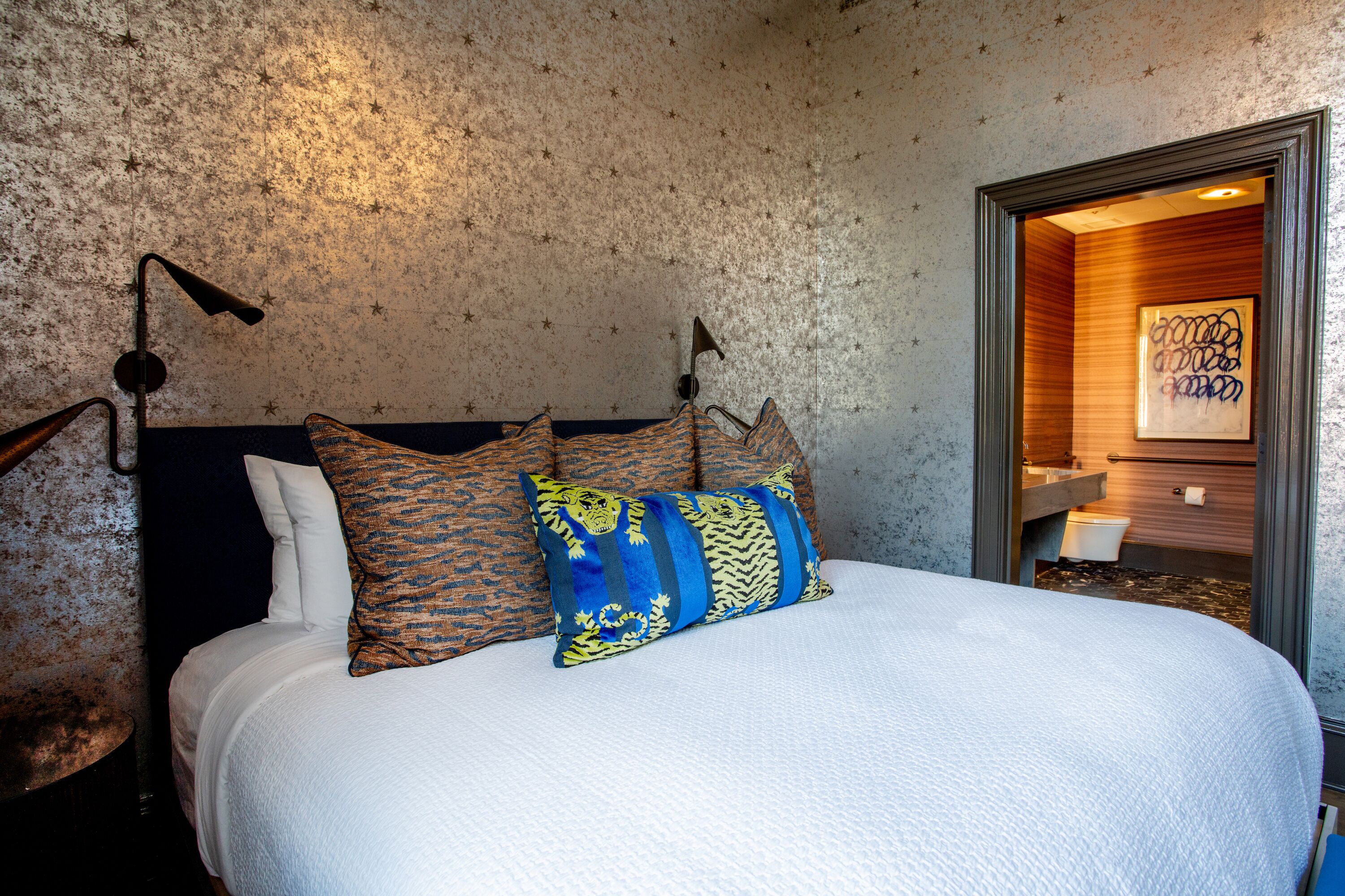 A bed with patterned pillows, a textured wall, and a framed artwork in the corner.