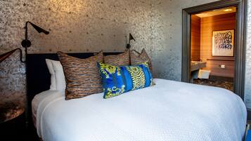 A bed with patterned pillows, a textured wall, and a framed artwork in the corner.