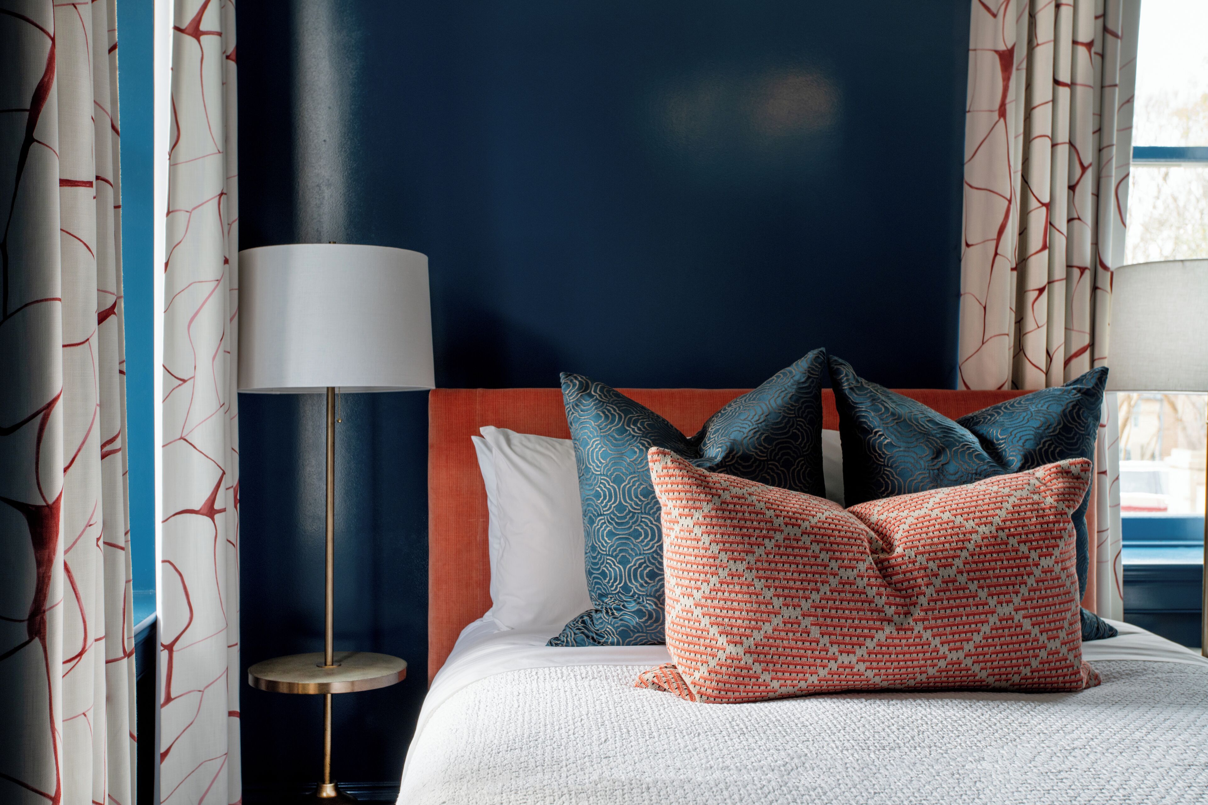 A hotel room with a bed, pillows, a lamp, and curtains.