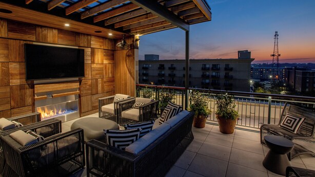 A rooftop terrace with a flat-screen TV, a fire feature, wicker furniture, and potted plants. - The Bell Athens by Kasa Living (Athens)