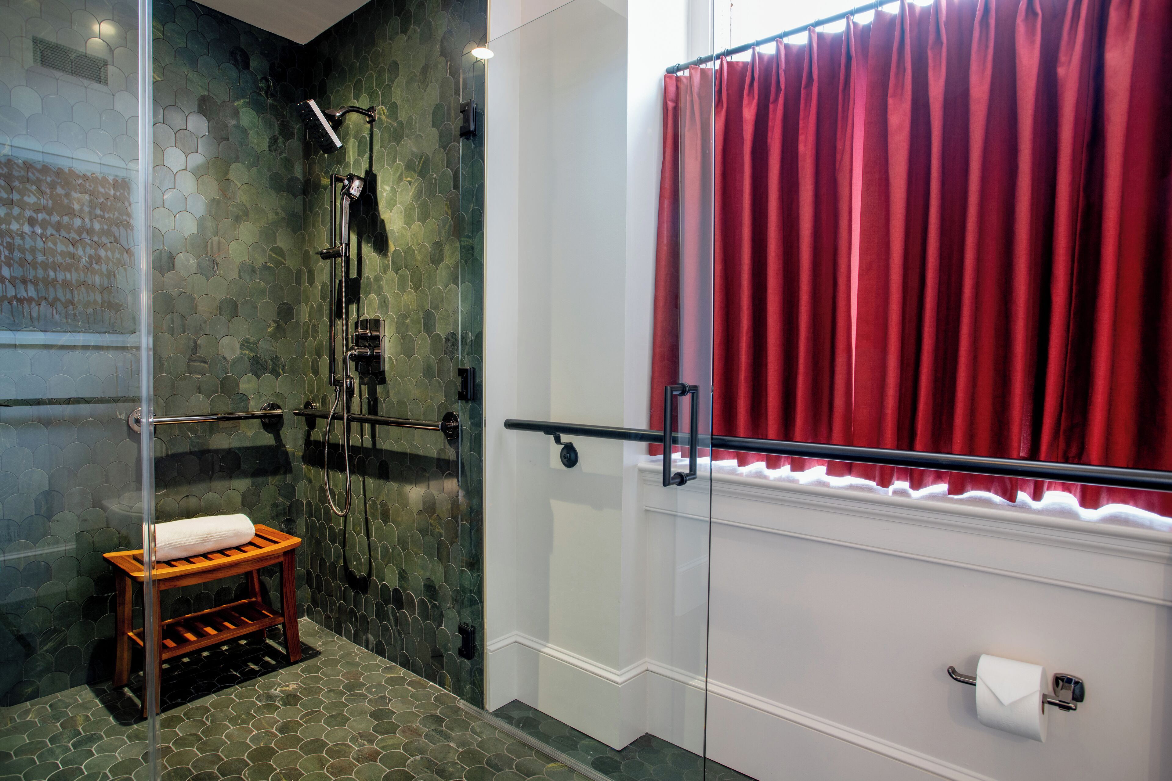 Une salle de bain moderne avec une douche à parois de verre, un tabouret en bois et un rideau rouge.