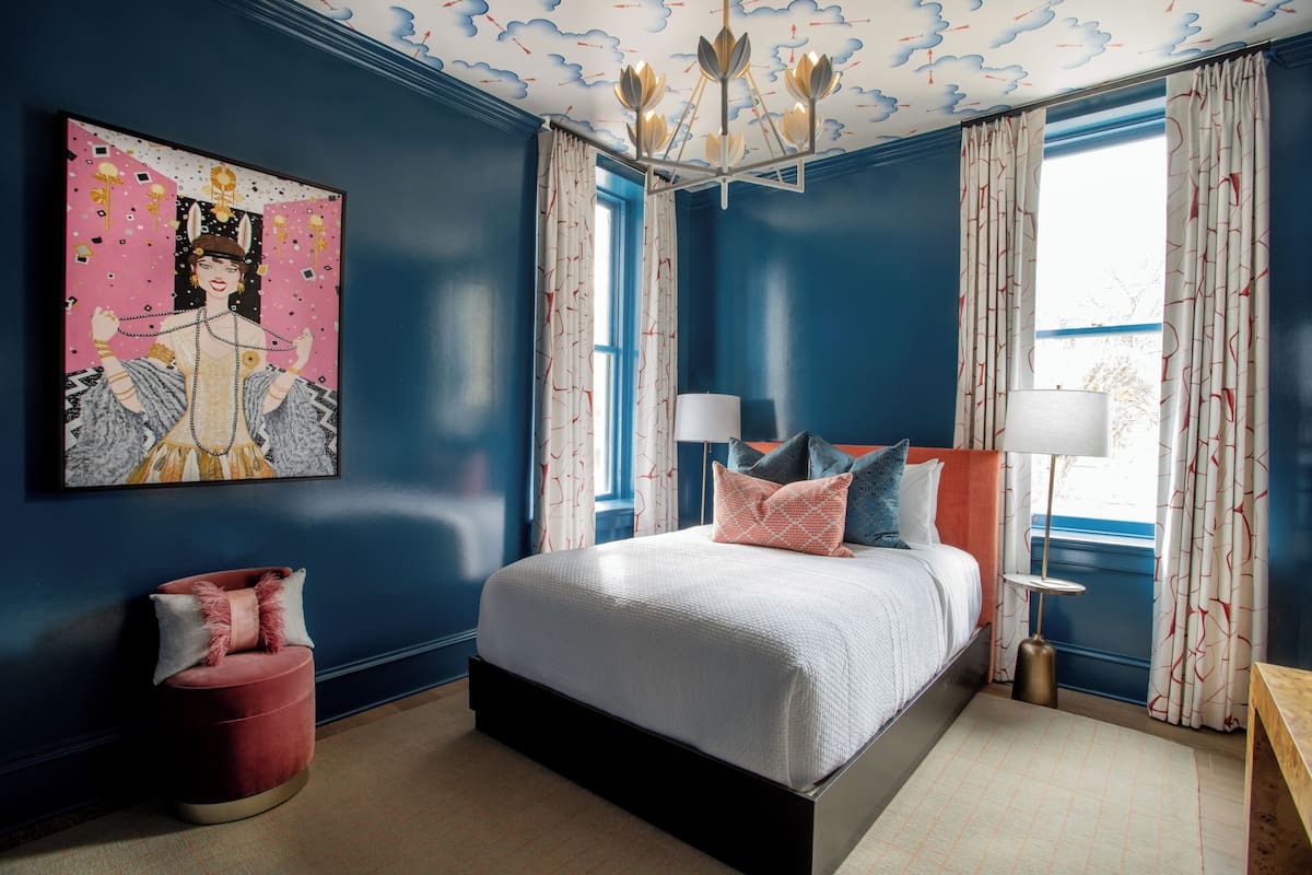 Un dormitorio con una cama grande, un reposapiés rojo, un techo con diseño floral y un cuadro en la pared.