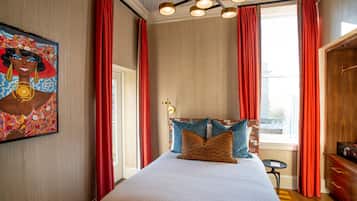 A hotel room with a large bed, red curtains, a painting on the wall, and a view of the city through the window.