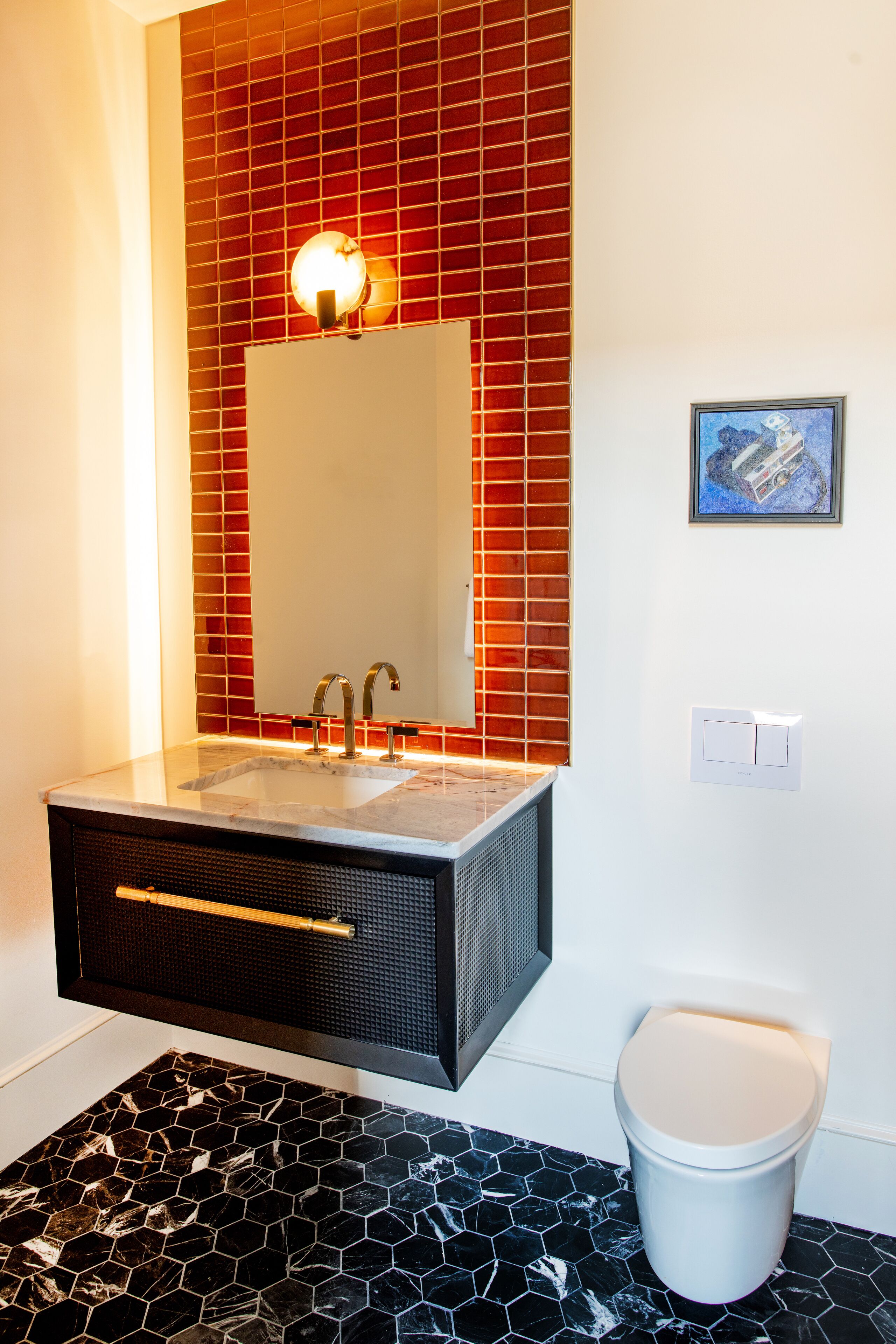 A bathroom with a rectangular sink, a mirror, a toilet, and a red tiled wall.