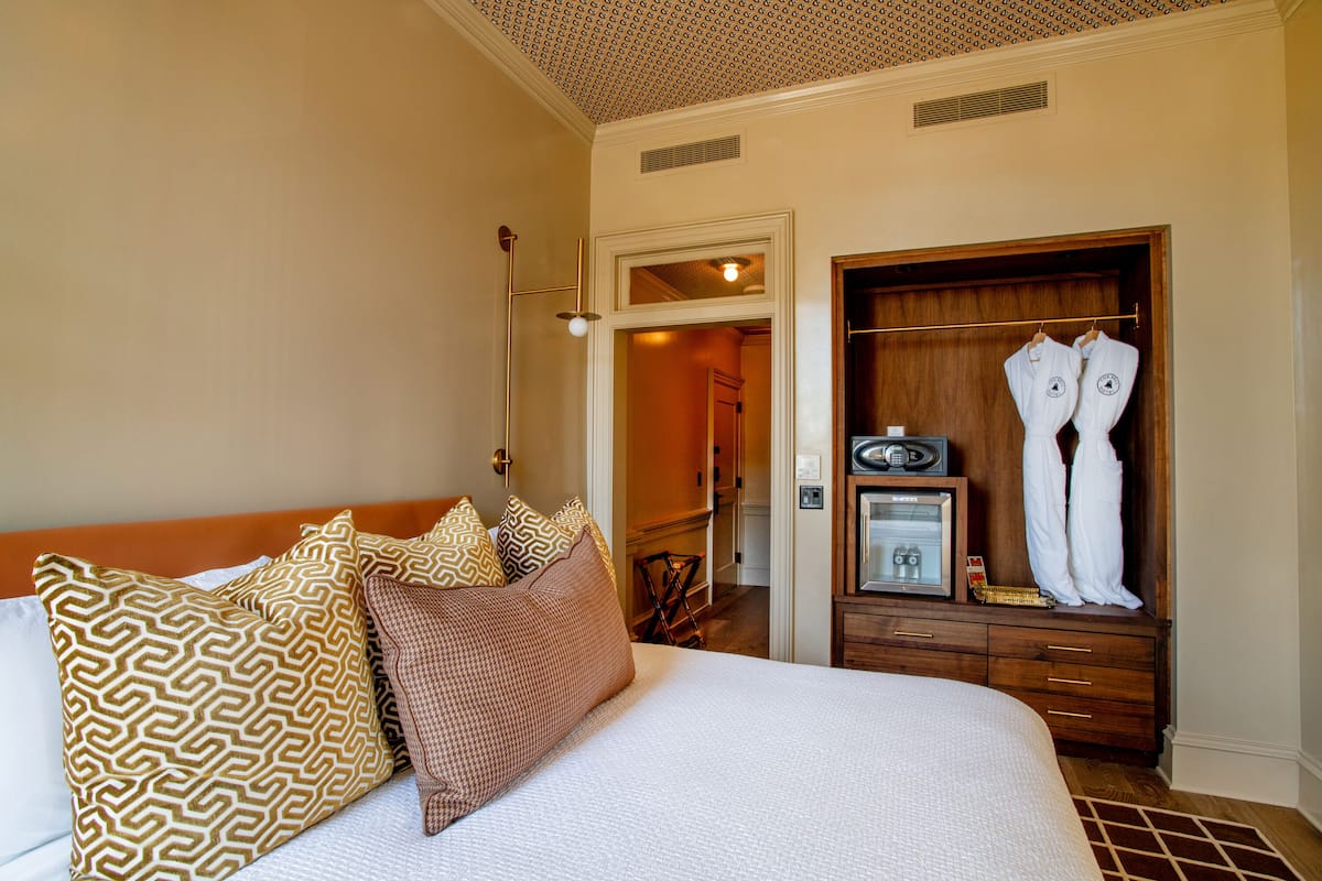 Habitación de hotel con una cama grande, almohadas estampadas, un aparador de madera y un vestidor con batas.