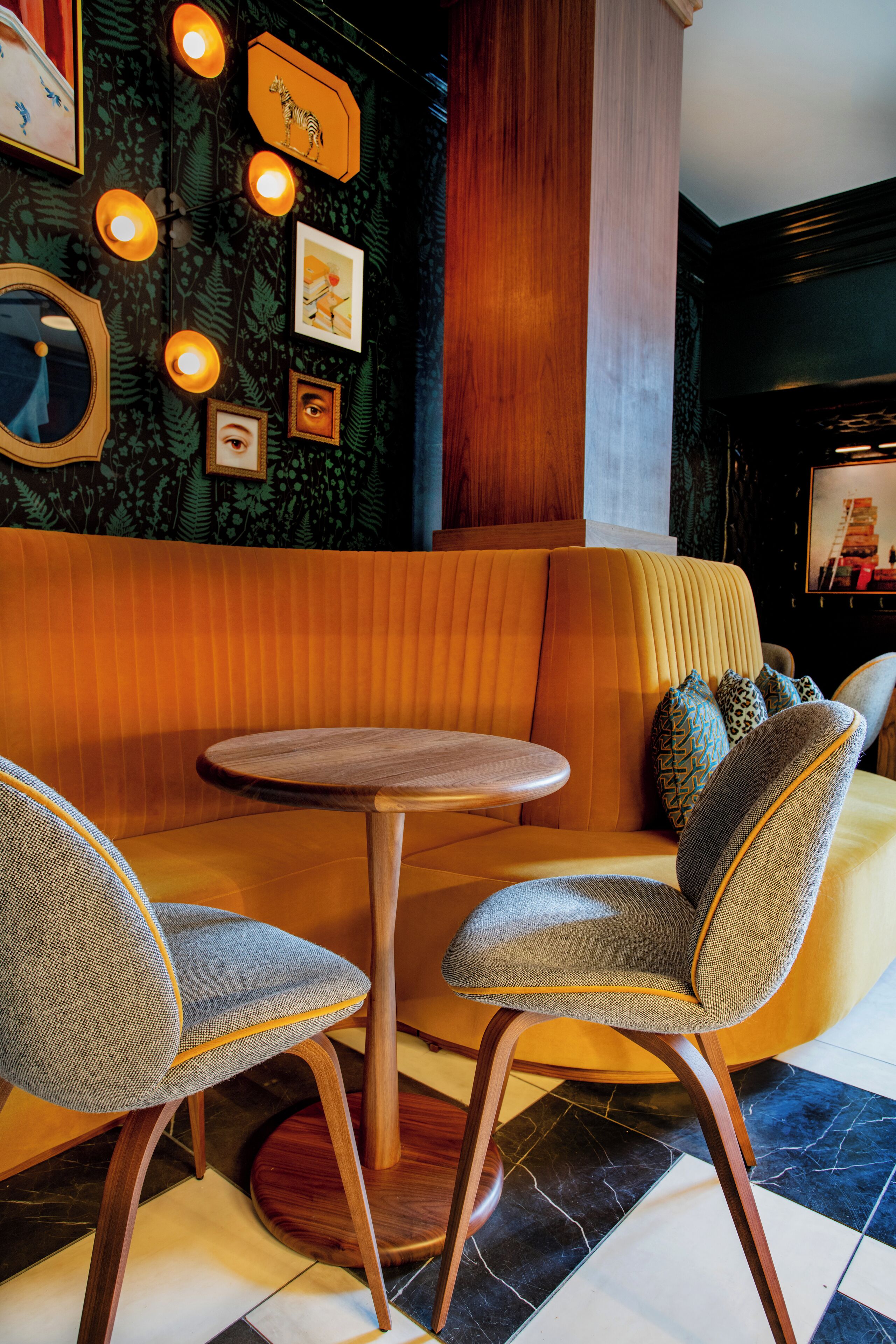 A cozy seating area with a round table and two chairs, a patterned wall, and framed pictures.