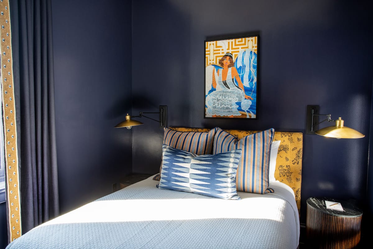 Una cama bien hecha con almohadillas a rayas, un cabecero con diseño estampado y un cuadro colgado en la pared.