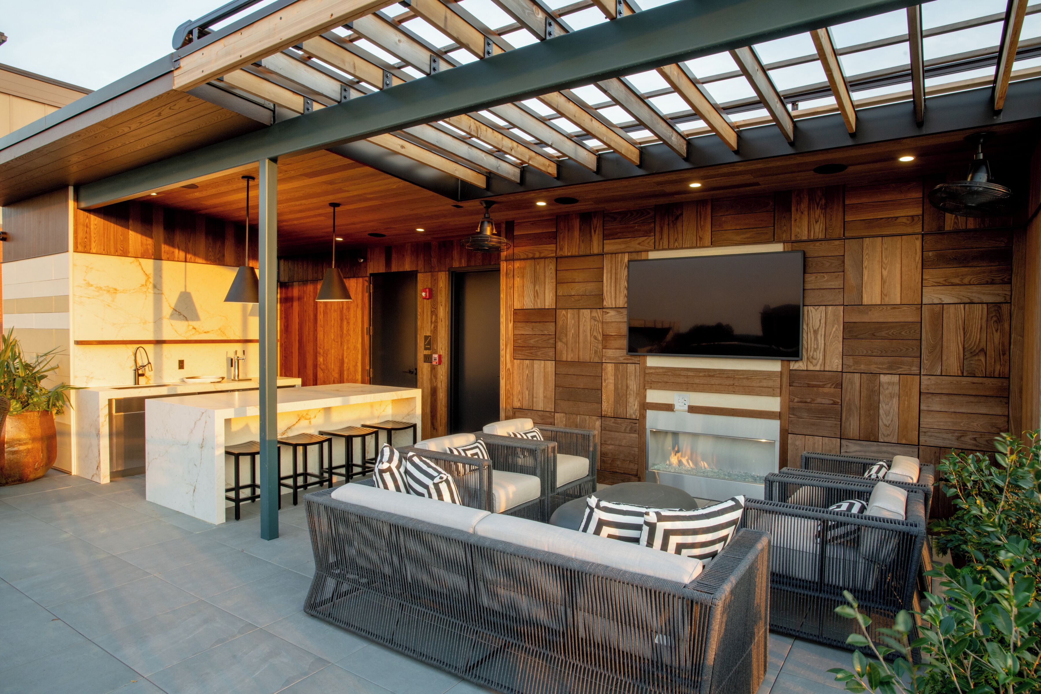 An outdoor patio with wicker furniture, a built-in kitchen, and a TV mounted on the wall.
