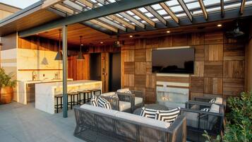 An outdoor patio with wicker furniture, a built-in kitchen, and a TV mounted on the wall.