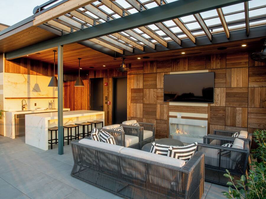 An outdoor patio with wicker furniture, a built-in kitchen, and a TV mounted on the wall.