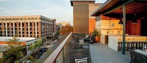 A rooftop terrace with outdoor seating, a bar area, and a view of the cityscape.