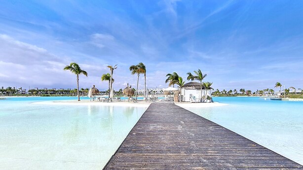 A wooden pier leading to a beach with clear turquoise water, palm trees, and a small building with a thatched roof. - Ground floor in front of the pool, south facing. (Torre Pacheco)