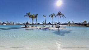 A clear blue pool surrounded by palm trees and a sandy beach. - Ground floor in front of the pool, south facing. (Torre Pacheco)
