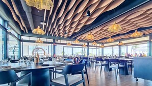 A modern restaurant with a unique ceiling design, large windows, and contemporary furniture. - Ground floor in front of the pool, south facing. (Torre Pacheco)