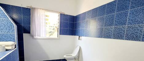 A bathroom with blue mosaic tiles, a toilet, a bidet, and a sink with a towel.