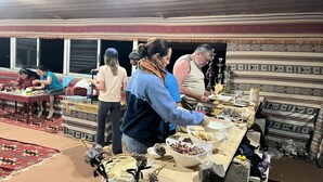 A communal dining area with a long table filled with food items and people serving themselves.