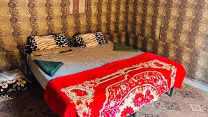 A bedroom with a bed, patterned wallpaper, and a red bedspread.