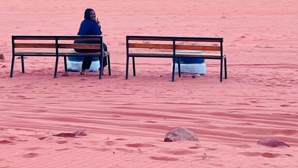Two wooden benches facing each other in a desert landscape with red sand and orange rock formations in the background.