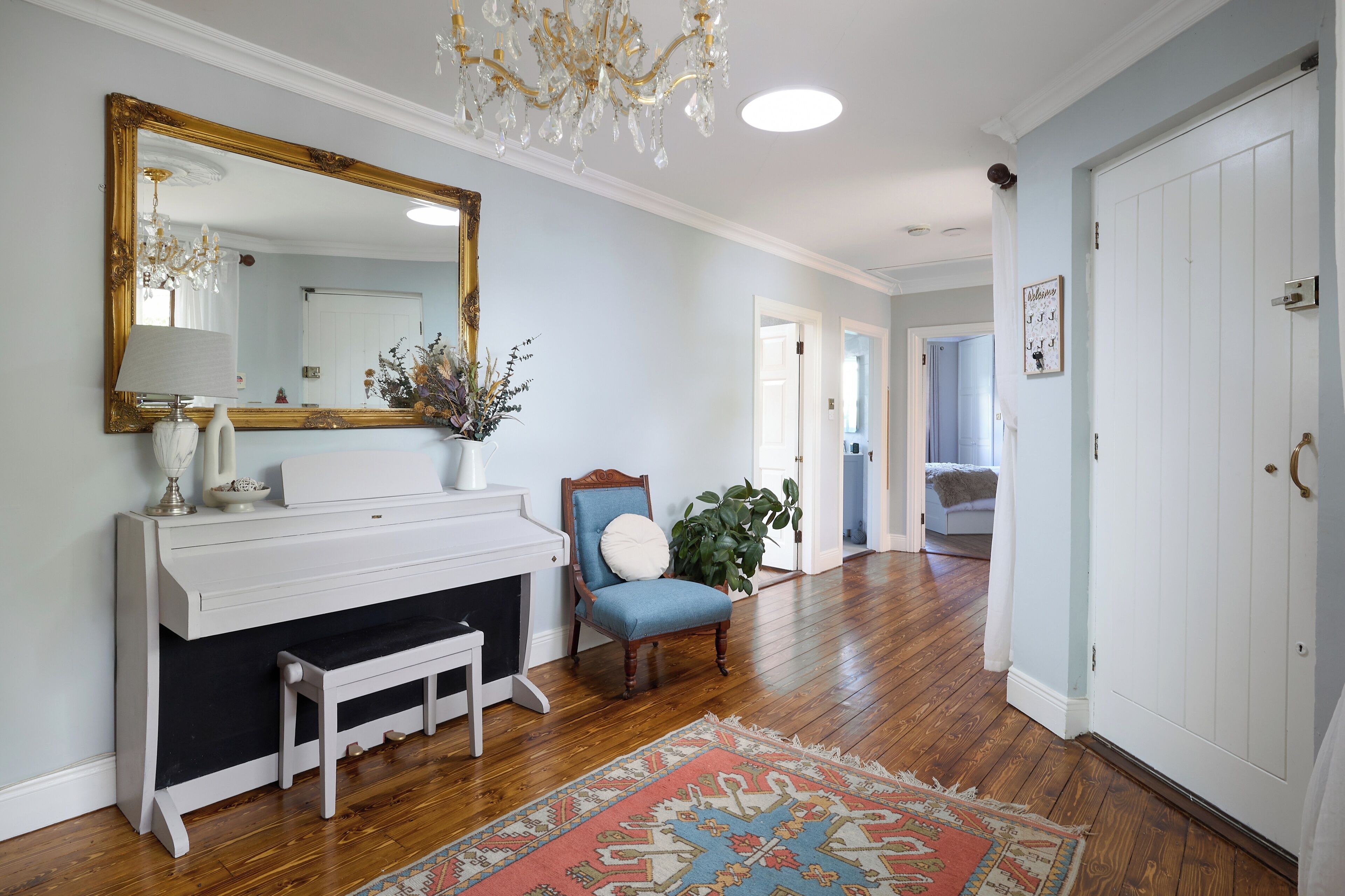 A room with a white piano, a blue armchair, a large mirror, and a wooden floor.