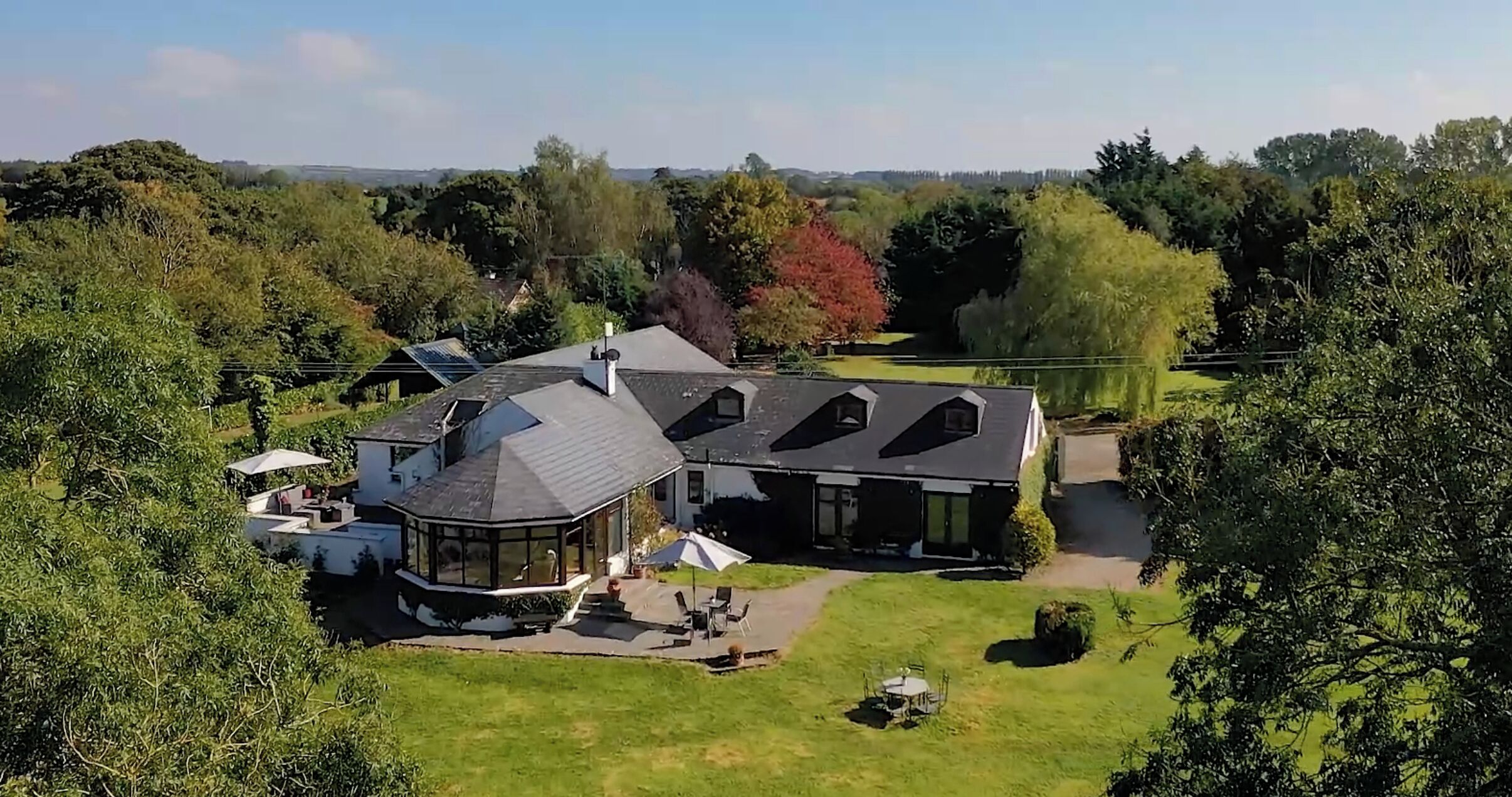 Une grande maison dotée d’une véranda en verre aux lignes courbes, d’un vaste patio et d’une pelouse bien entretenue.