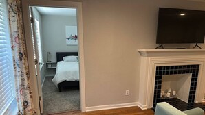 A hotel room with a bed, a TV, a fireplace, and a door leading to another room. - Rt 66 Retreat - Near Fairgrounds (Tulsa)