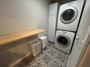 A laundry room with a washing machine, dryer, and a small trash bin.