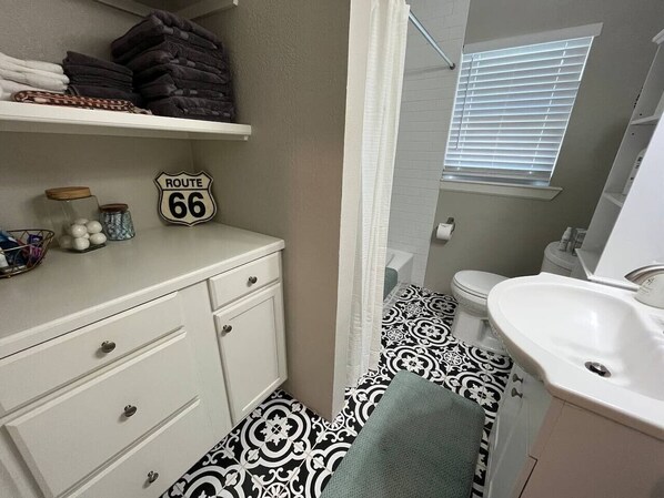 Un baño con piso de diseño blanco y negro, lavamanos blanco, tocador blanco y un perchero para toallas.