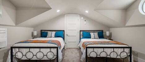 A bedroom with two beds, a white door, and a sloped ceiling with recessed lighting.