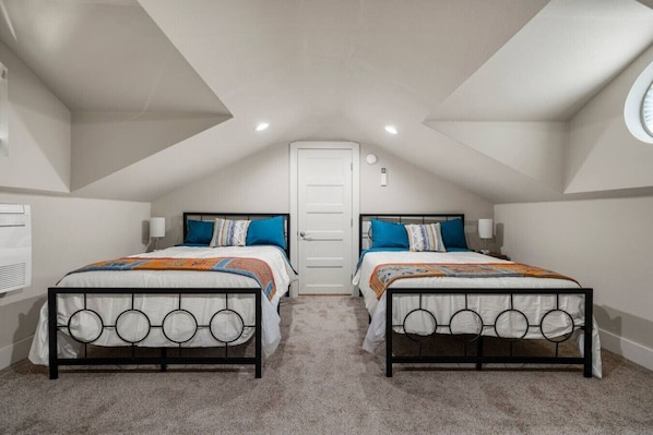 A bedroom with two beds, a white door, and a sloped ceiling with recessed lighting.