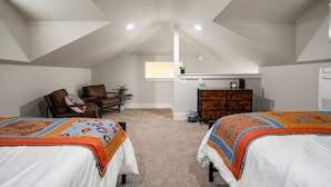 A bedroom with two beds, a desk, a chair, and a small kitchenette.